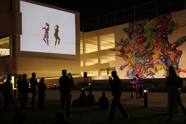 Installation view of a plaza with dancers and projections.
