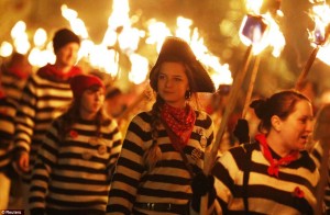 photo of people in striped shirts and pirate hats walking with torches in the night